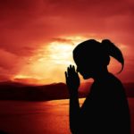 woman meditating or praying with deep red sunset in background photo