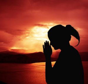 woman meditating or praying with deep red sunset in background photo